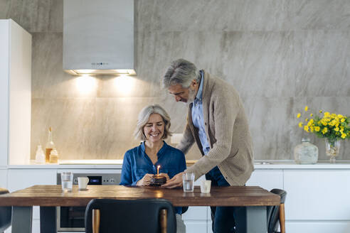 Mature couple celebrating birthday with cake in kitchen at home - SODF00582