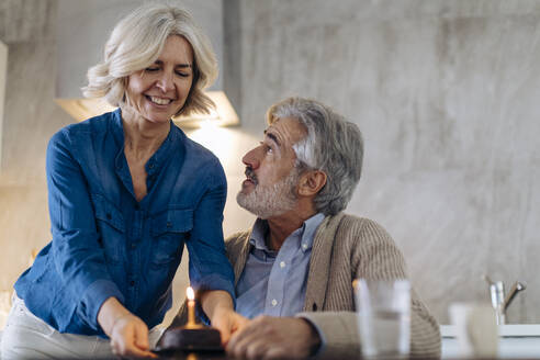 Mature couple celebrating birthday with cake in kitchen at home - SODF00589