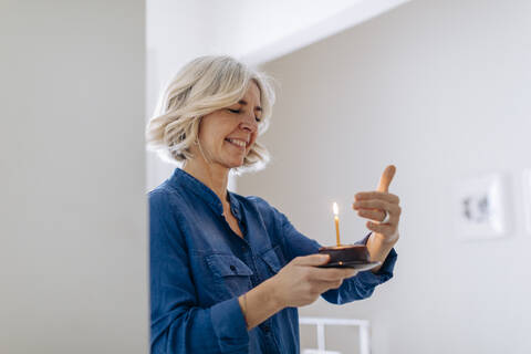 Glückliche reife Frau mit Geburtstagskuchen zu Hause, lizenzfreies Stockfoto