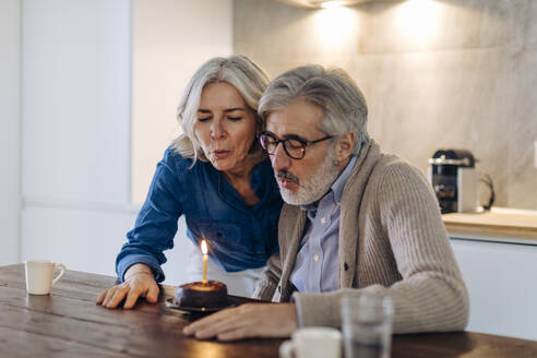 Mature couple celebrating birthday with cake in kitchen at home - SODF00595