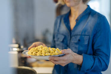 Close-up of woman holding a plate with tortellini in kitchen at home - SODF00604