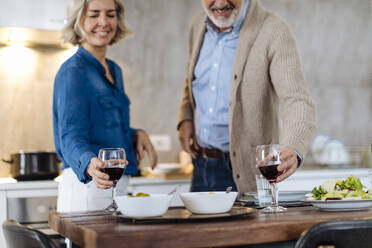 Reifes Paar erhebt Weingläser beim Abendessen in der Küche zu Hause - SODF00607