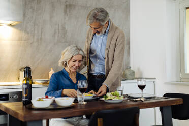 Mature man serving dinner to his wife in kitchen at home - SODF00613