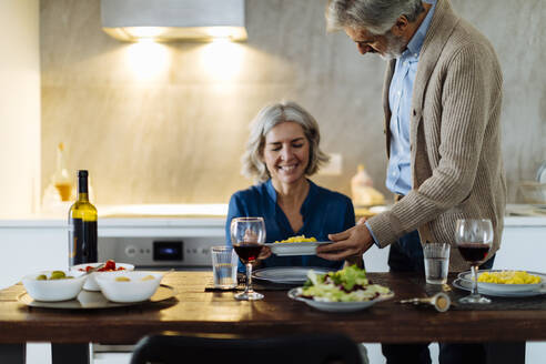 Älterer Mann serviert seiner Frau in der Küche zu Hause das Abendessen - SODF00615