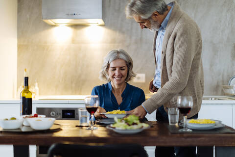 Älterer Mann serviert seiner Frau in der Küche zu Hause das Abendessen, lizenzfreies Stockfoto