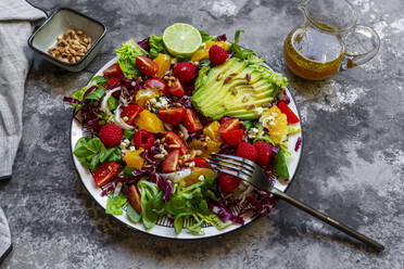 Studioaufnahme eines fruchtigen Salattellers mit Feldsalat, Radicchio, Salatherzen, Avocado, Tomaten, Pinienkernen, Himbeeren, Orangen und Limetten - SARF04430