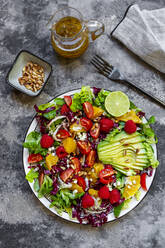 Studioaufnahme eines fruchtigen Salattellers mit Feldsalat, Radicchio, Salatherzen, Avocado, Tomaten, Pinienkernen, Himbeeren, Orangen und Limetten - SARF04431