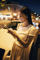 Lächelnde Frau mit Smartphone in der nächtlichen Stadt - OYF00094