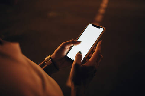 Hände einer Frau, die nachts ein Smartphone hält, Nahaufnahme, lizenzfreies Stockfoto