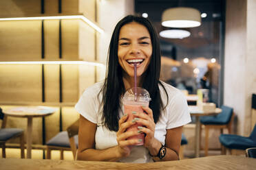 Black-haired woman drinking a smoothie in cafe - OYF00107