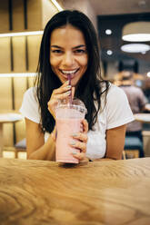 Black-haired woman drinking a smoothie in cafe - OYF00111