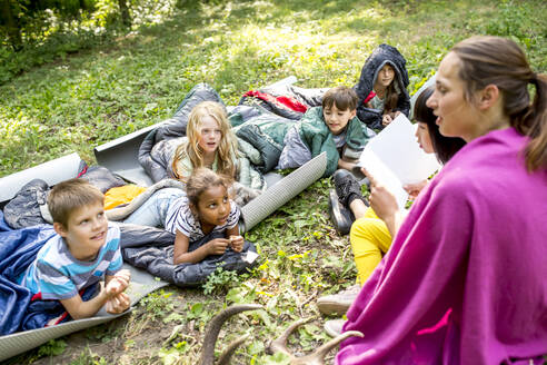 Lehrerin liest Schulkindern beim Zelten im Wald eine Geschichte vor - WESTF24486