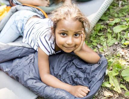 Kleines Mädchen liegt auf einem Schlafsack und schaut in die Kamera - WESTF24487