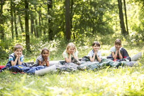 kinder zelten im Wald, in ihren Schlafsäcken sitzend, lizenzfreies Stockfoto