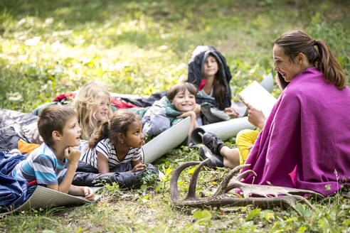 Lehrerin liest Schulkindern beim Zelten im Wald eine Geschichte vor - WESTF24557