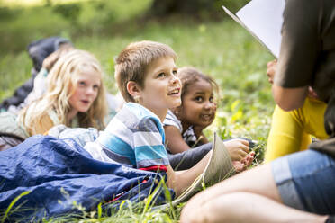 Teacher reading story to school children, camping in the forest - WESTF24558