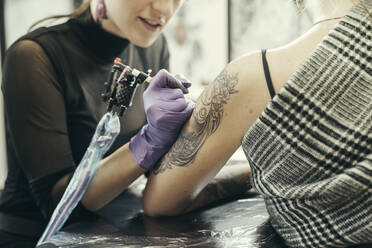 female tattooist tattooing upper arm of female customer - MTBF00332