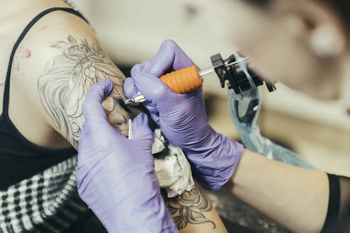 female tattooist tattooing upper arm of female customer - MTBF00333