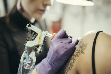 female tattooist tattooing upper arm of female customer - MTBF00334