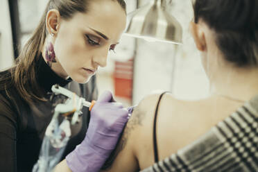 female tattooist tattooing upper arm of female customer - MTBF00335