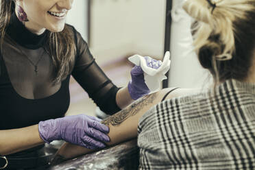 female tattooist tattooing upper arm of female customer - MTBF00339