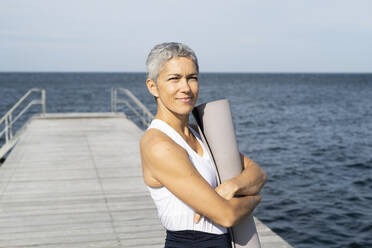 Frau hält Yogamatte auf Pier - JOHF05491