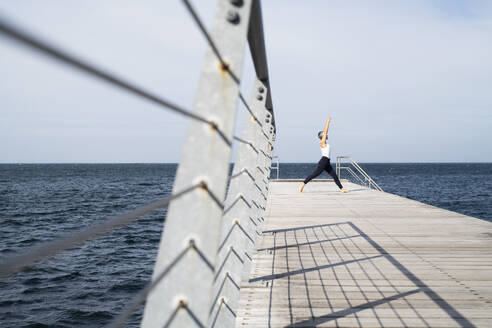 Woman practicing yoga on pier - JOHF05496