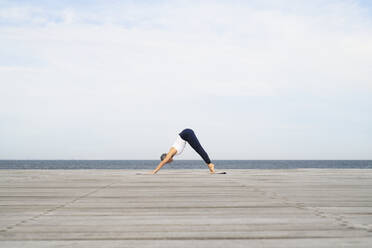 Woman practicing yoga on pier - JOHF05502