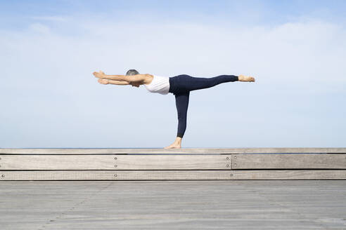 Woman practicing yoga on pier - JOHF05506