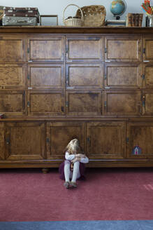 Unhappy little girl sitting on the floor in front of big cabinet - PSIF00366