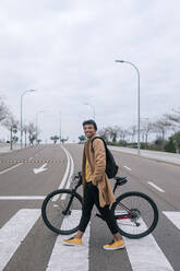 Junger Mann mit Fahrrad beim Überqueren einer Straße in der Stadt - GRCF00084