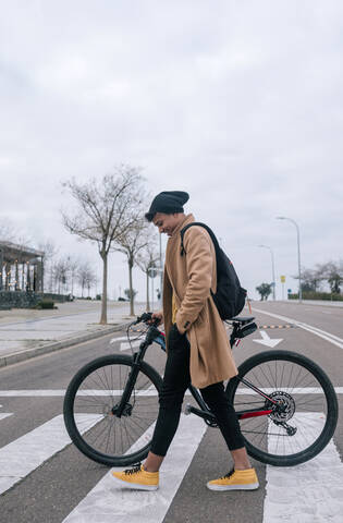 Junger Mann mit Fahrrad beim Überqueren einer Straße in der Stadt, lizenzfreies Stockfoto