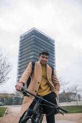 Porträt eines lächelnden jungen Mannes mit Fahrrad in der Stadt - GRCF00088