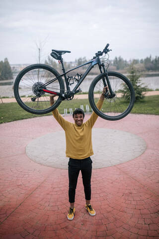 Porträt eines glücklichen jungen Mannes, der ein Fahrrad anhebt, lizenzfreies Stockfoto