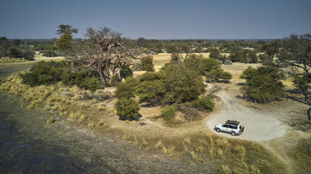 Luftaufnahme eines isolierten weißen Jeeps auf einer schmutzigen Piste und eines großen Baobab-Baums, Bwabwata National Park, Namibia - VEGF01416