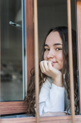 Porträt eines lächelnden Teenagers, der aus dem Fenster schaut - DLTSF00408