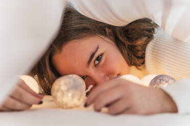 Portrait of teenage girl with chain of lights underneath bedcover - DLTSF00412