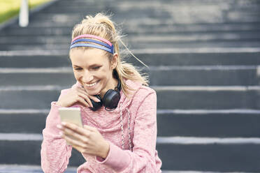 Sportliche Frau sitzt auf einer Treppe und benutzt ihr Smartphone - ABIF01241