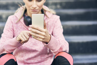 Sportliche Frau sitzt auf einer Treppe und benutzt ihr Smartphone - ABIF01242