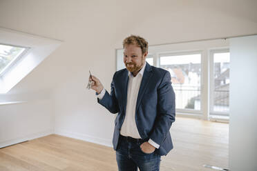Portrait of smiling businessman standing in empty apartement holding key - GUSF03182