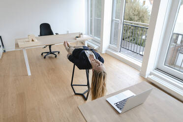 Junge Geschäftsfrau übt Yoga im Büro auf einem Hocker liegend - GUSF03190