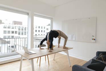 Young businesswoman practicing yoga on desk in office - GUSF03192