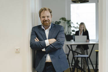 Portrait of confident businessman in office with businesswoman in background - GUSF03202