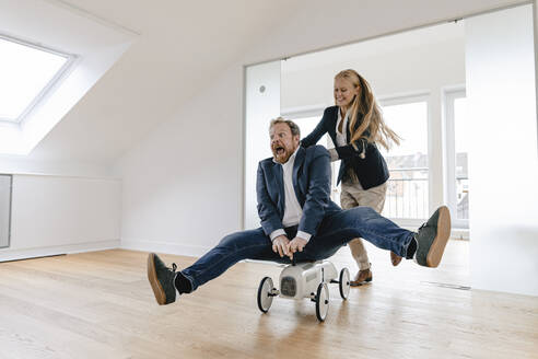 Playful businesswoman pushing businessman on toy car in office - GUSF03214