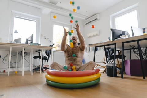 Crazy businessman sitting in wading pool in office playing with balls stock photo