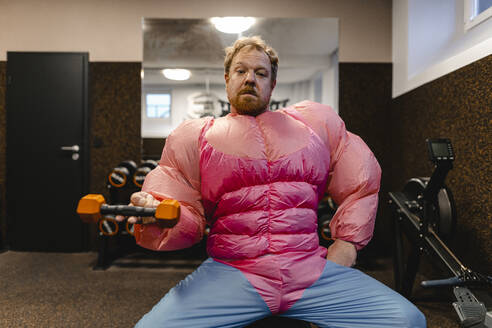 Man in gym wearing pink bodybuilder costume lifting dumbbell - GUSF03222