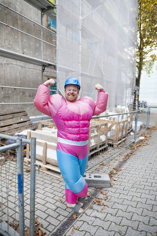 Porträt eines stolzen Mannes in rosa Bodybuilder-Kostüm und Schutzhelm auf einer Baustelle, lizenzfreies Stockfoto