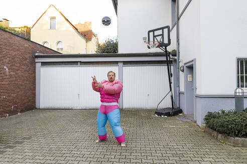 Porträt eines Mannes mit Basketball im rosa Bodybuilder-Kostüm - GUSF03230