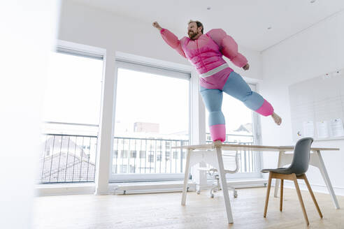 Businessman in office wearing pink bodybuilder costume pretending to fly - GUSF03231