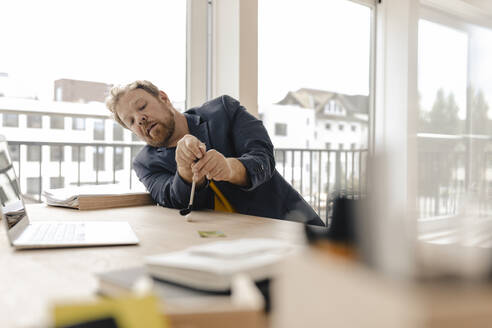 Geschäftsmann spielt Golf auf dem Schreibtisch im Büro - GUSF03239